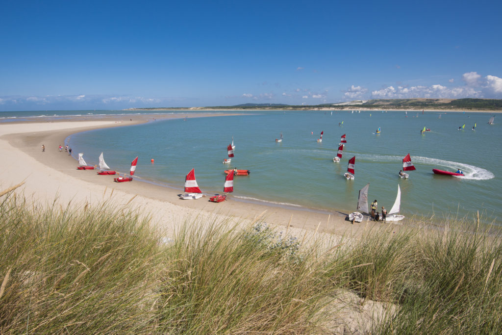 from sand dunes onto beach with many small sailing boats and children learning to sail at Le Touquet Paris-Plage