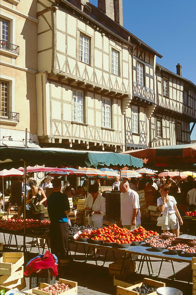 Chalon-sur-Saone market with old wooden houses in background and colourful stalls with fruit and vegetables and people in front