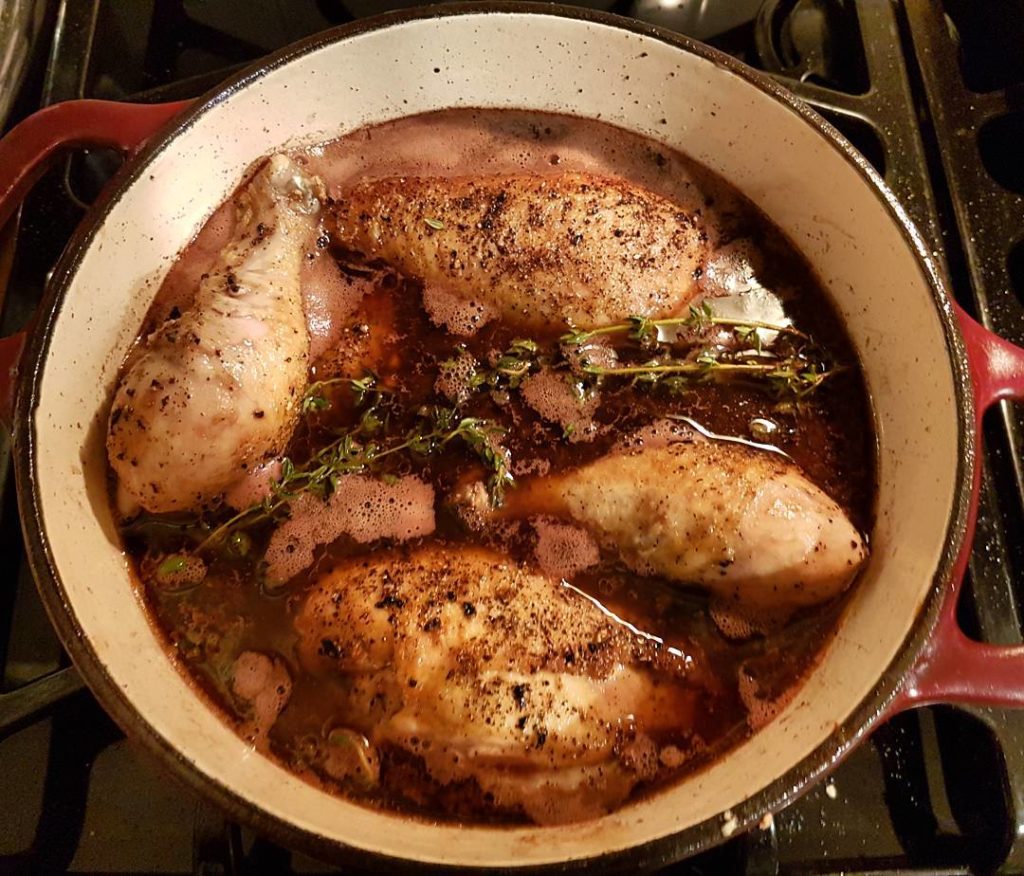 pieces of chicken in a coq au vin in a round pot