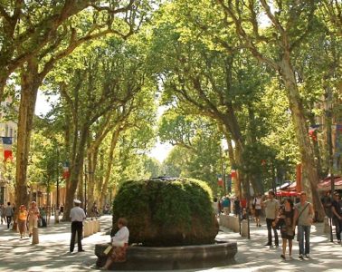 Tree lined pedestrian street in Provence with cafes and people and central fountain