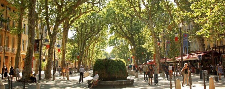 Tree lined pedestrian street in Provence with cafes and people and central fountain