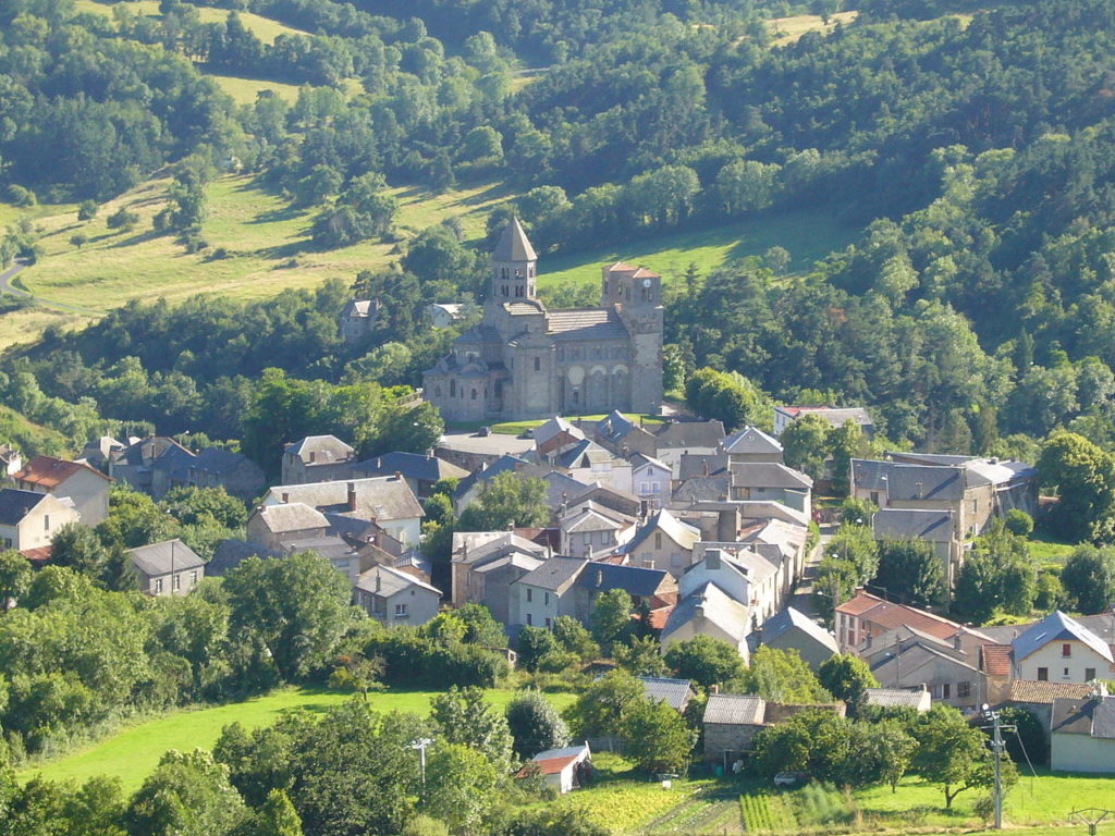 Aerial view of St Nectaire with its cathedral in the distance and houses around. All in full countryside.