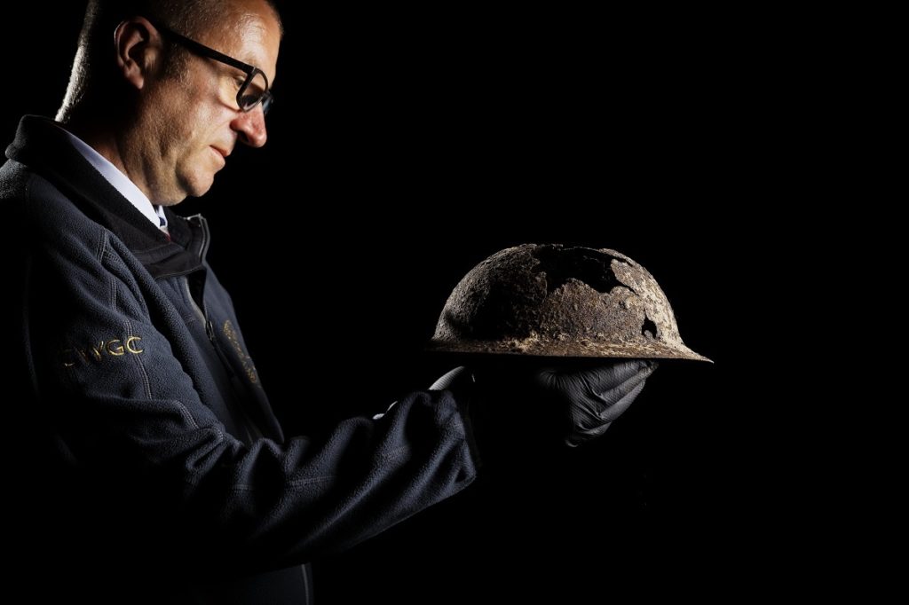 Man standing holding a battered World War I helmet at the CWGC Recovery and Reburial section