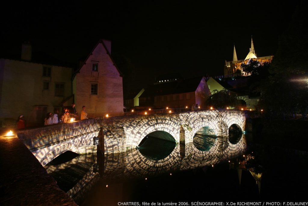Chartres lit up with bridge illuminated and people walking across river