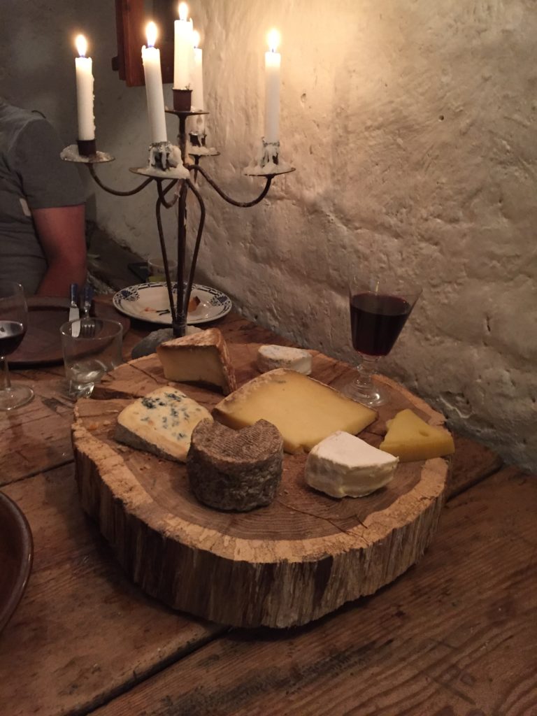 Cheeses on a block of wood with candles behind and glass of wine
