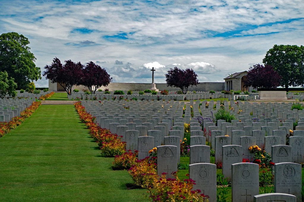 Serre Road CWGC cemetery with flowers beside large number of graves and cross in distance