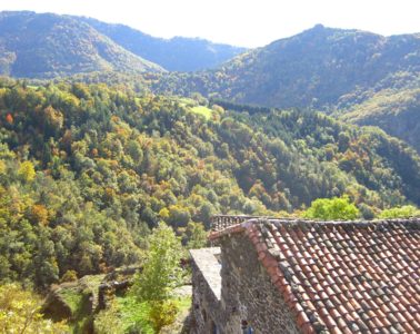 View over river valley and highhills in the distance and red-rooved house below