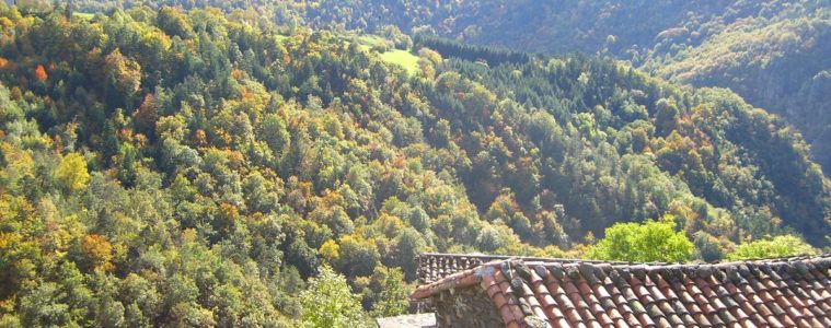 View over river valley and highhills in the distance and red-rooved house below