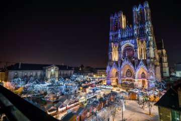 Reims christmas Market aerial view looking at cathedral inthe distance and square lit up with lights, stalls and people