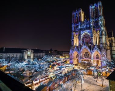 Reims christmas Market aerial view looking at cathedral inthe distance and square lit up with lights, stalls and people