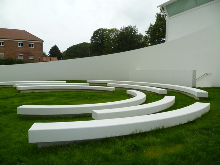 Wilfred owen memorial with white wall behind and circular white concrete maze on green ground below