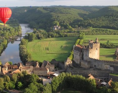 red montgolfiere balloon way above old warm stone chateau on the banks of the Dordogne River