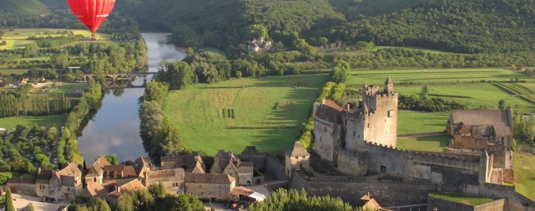 red montgolfiere balloon way above old warm stone chateau on the banks of the Dordogne River