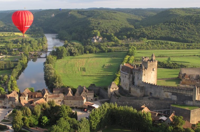 red montgolfiere balloon way above old warm stone chateau on the banks of the Dordogne River