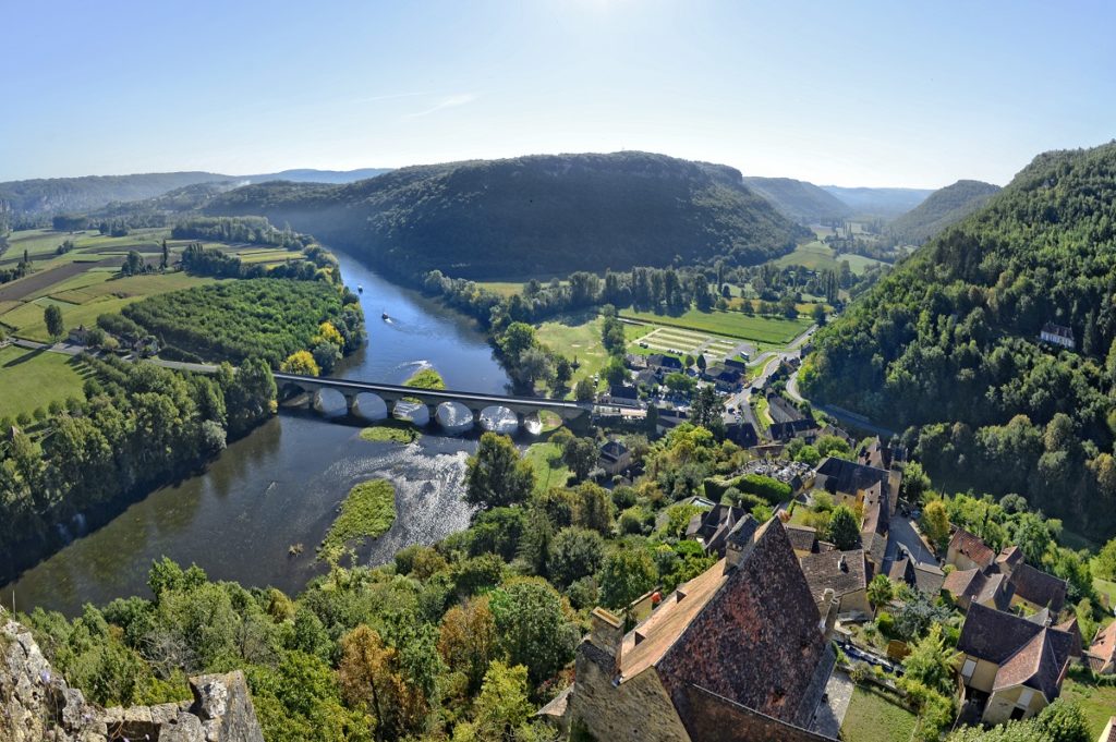 Overhead view of Perigord Dordogne Valley with red rooves in front, hillsides of trees, stone bridge over the Dordogne River