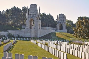 Etaples Military Cemetery with two memorial gates in background and ranks of graves in foreground in unusual perspective