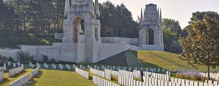 Etaples Military Cemetery with two memorial gates in background and ranks of graves in foreground in unusual perspective