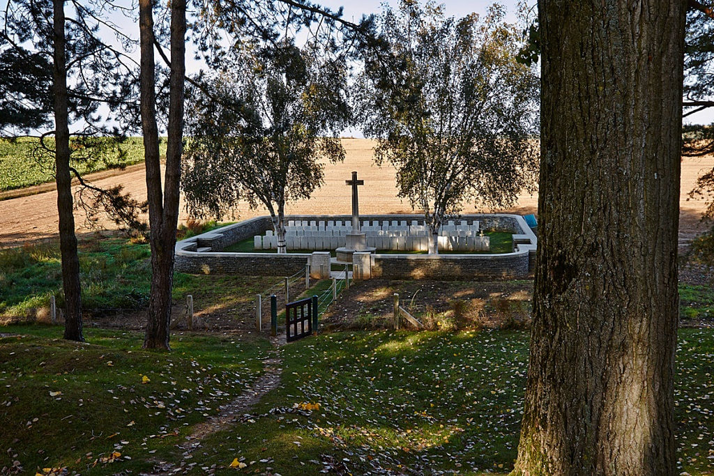 Railway HOllow Military Cemetery at dusk. Small military cemetery with trees shading a walled cemetery with cross in background