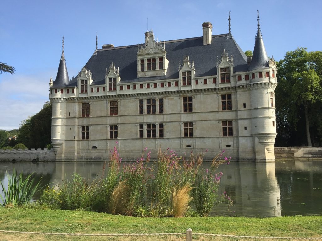 azay-le-rideau chateau facade seen from the other side of the moat with turrets, white stone building and greenery in front