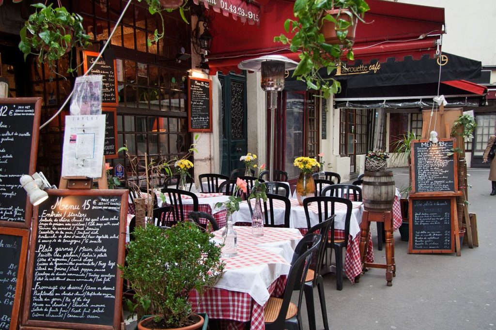 Restaurant in rue Mouffetard, Paris outside terrace with board at front listing 15 euro menu and tables laid with white cloths, and lots of greenery