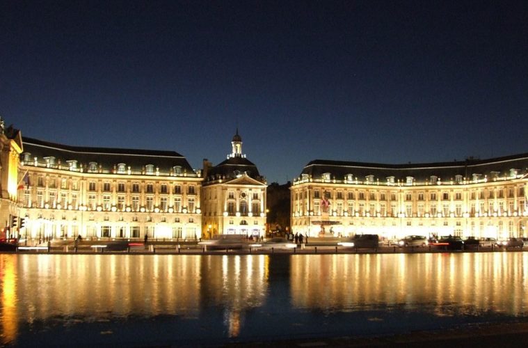 Place de la Bourse in Bordeaux at night, with neo-classical building in a semi circle looking out over water and reflected in it