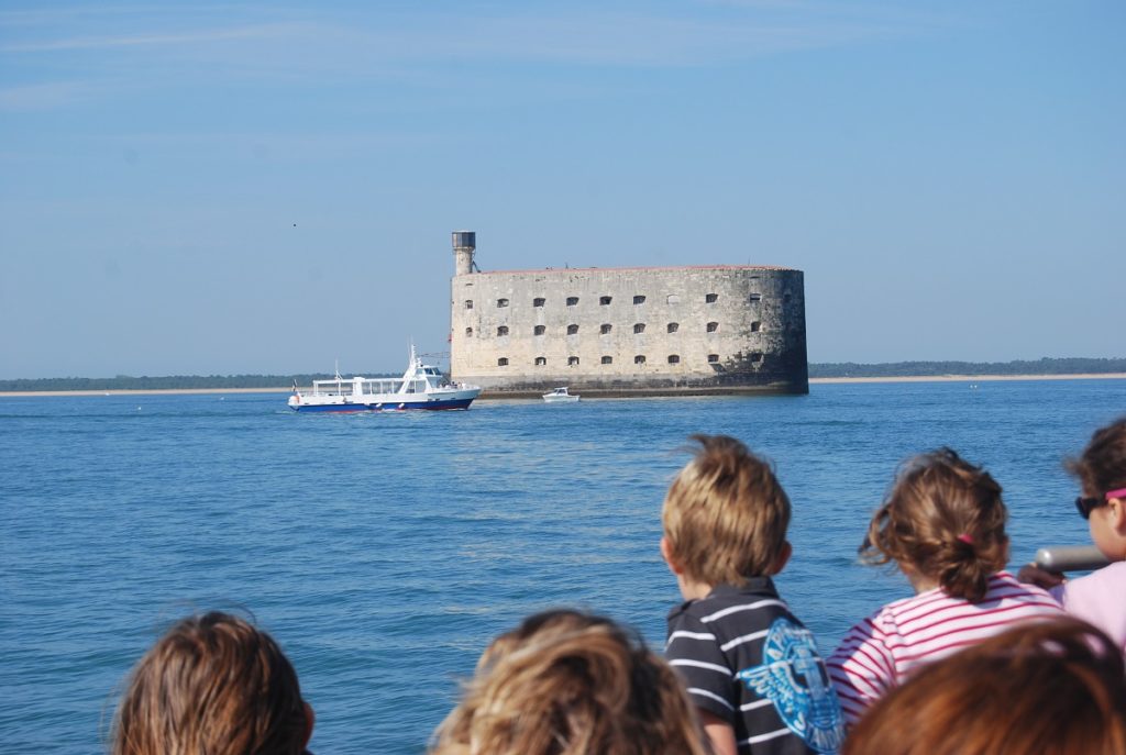 Heads of children on boat at sea looking at Fort Boyard, a vast prison