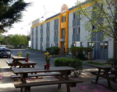 Look at premiere classe budget hotel from side with tables and chairs outside.