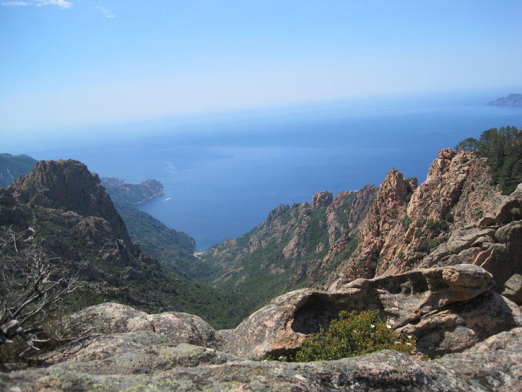View fromthe top of the mountain range in Corsica towards the blue sea with rocky mountains and little vegetation