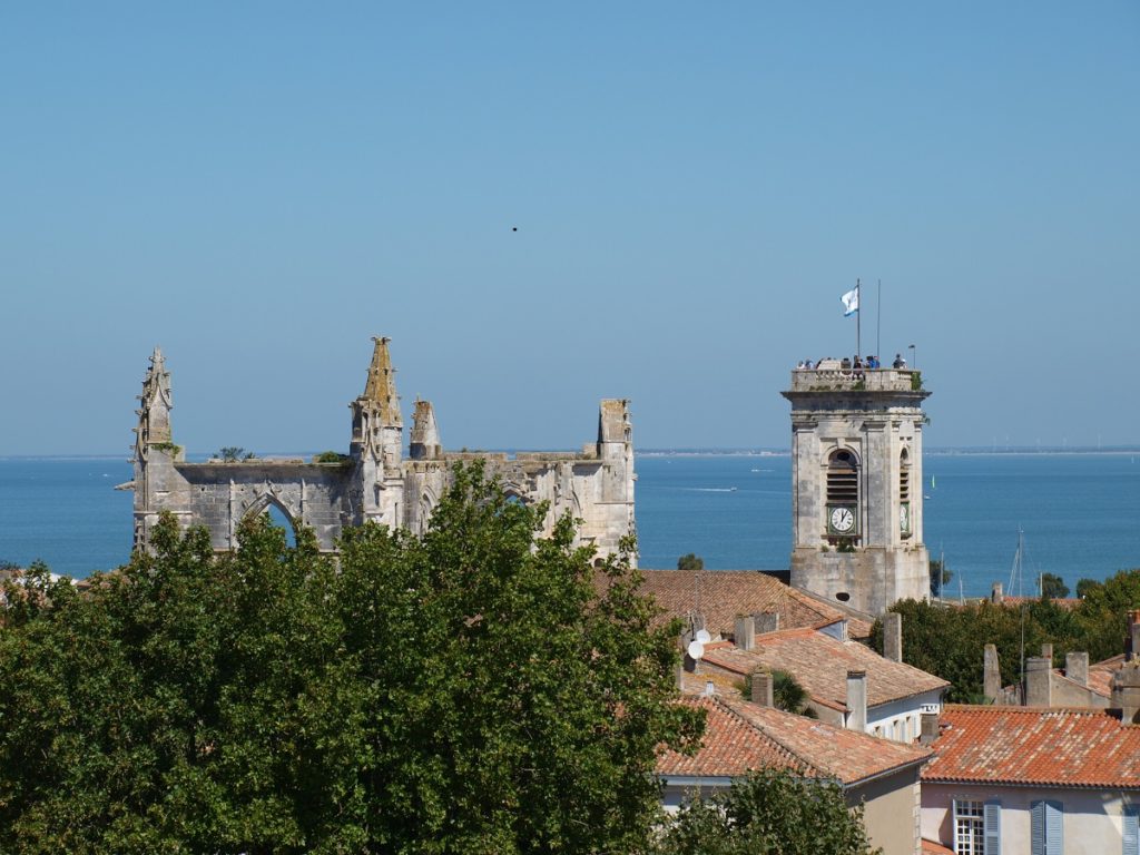 Ile de Ré village looking at church tower and castle ruins from tower level with trees in front and sea in background