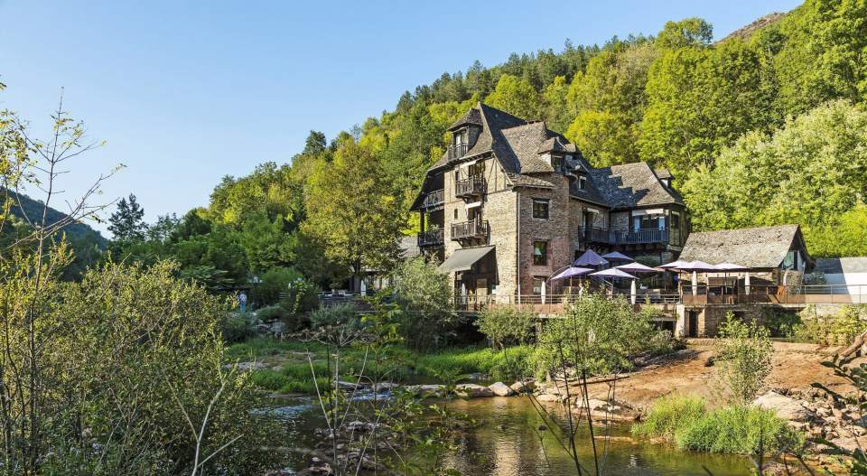 Domaine Cambelong in Conques, a tall former mill beside a gently flowing river in teh valley with wooded hillside behind