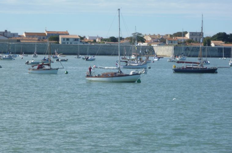 Ile d'Aix harbour looking fromthe sea to yachts bobbing upand down, with defensive walls and houses behind in the harbour