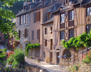 Old 3-storey houses up a street with half timering, stone rooves and greenery