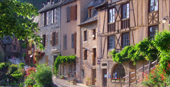 Old 3-storey houses up a street with half timering, stone rooves and greenery