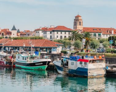 From the water looking at the small harbour of St Jean de Luz on the French Atlantic coast with red rooved buildings in background and tall tower and boats in foreground