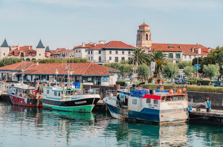 From the water looking at the small harbour of St Jean de Luz on the French Atlantic coast with red rooved buildings in background and tall tower and boats in foreground