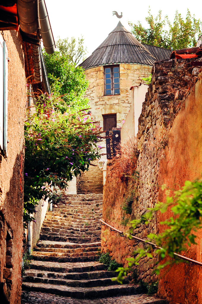 View from bottom of cobbled steps in steep narrow passaagemway leading up to warm pink house in Lautrec Village