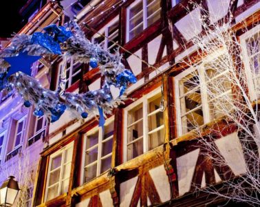 Strasbourg street at christmas with half timbered houses lit up in background, tree branch to right and big decoration hung in street in front