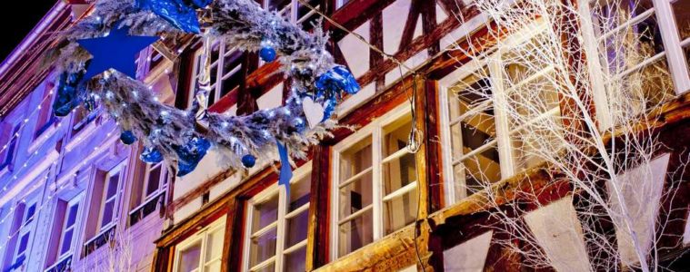 Strasbourg street at christmas with half timbered houses lit up in background, tree branch to right and big decoration hung in street in front