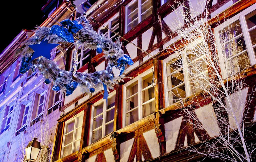 View up to half-timbered houses in Strasbourg at Christmas with silver and blue wreath hanging from wire and white painted branches