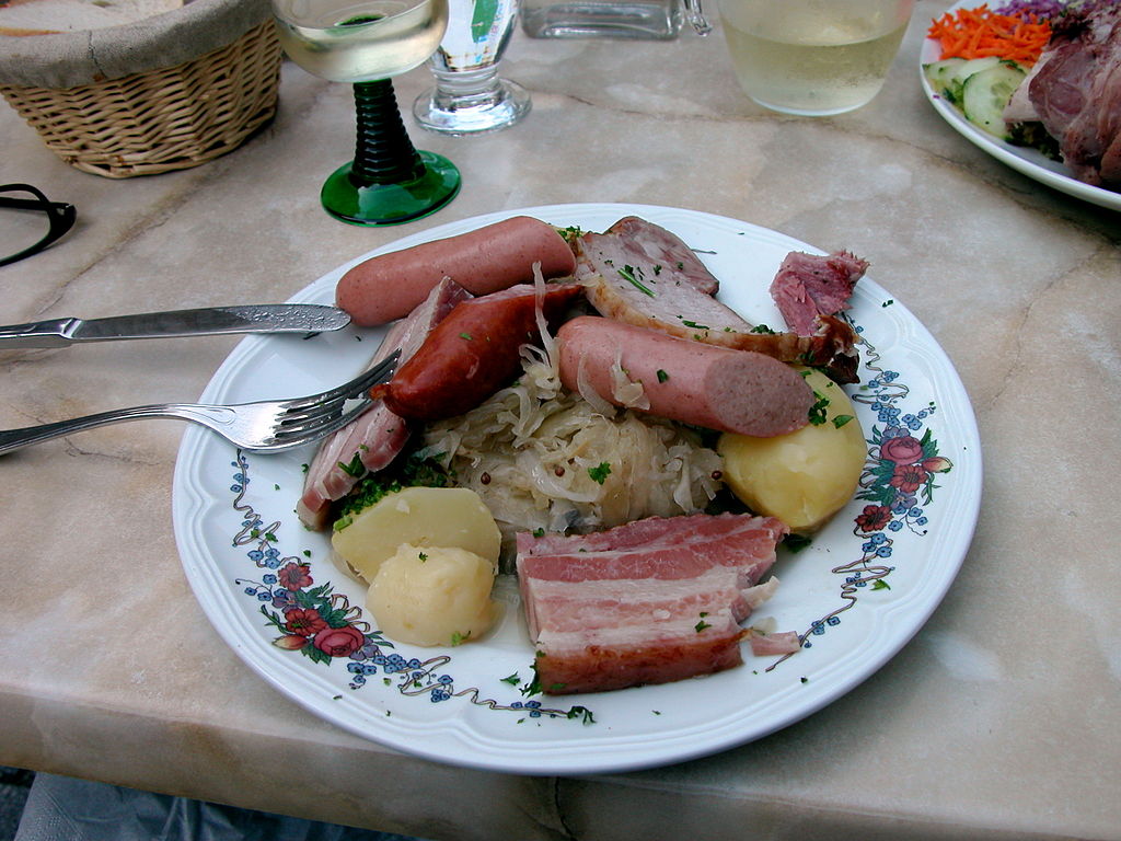 Plate of Alsation Choucroute Food of France with plate piled with ham, potatoes, sausages and vegetables, with glas of wine in background