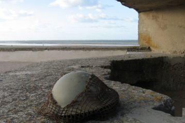 Soldier's helmet on beach at entrance to concrete bunker looking out to sea