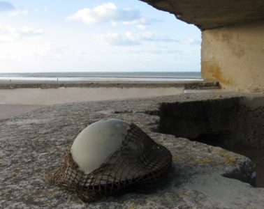Soldier's helmet on beach at entrance to concrete bunker looking out to sea