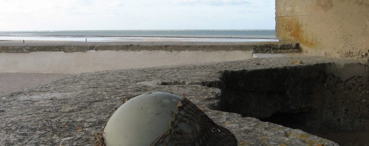 Soldier's helmet on beach at entrance to concrete bunker looking out to sea