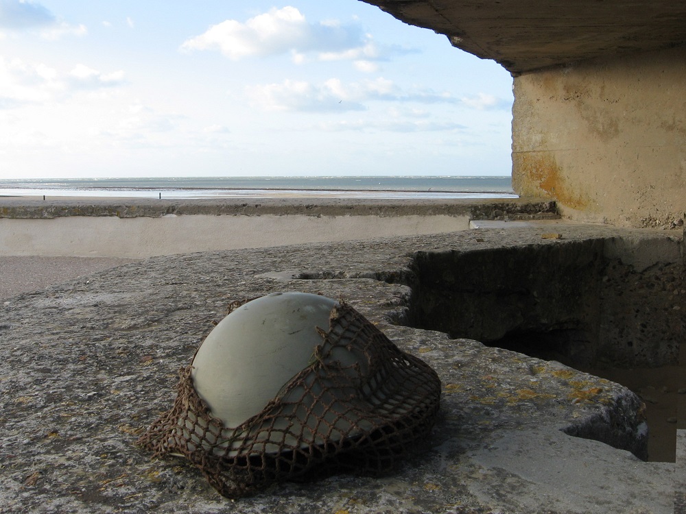 Soldier's helmet on beach at entrance to concrete bunker looking out to sea