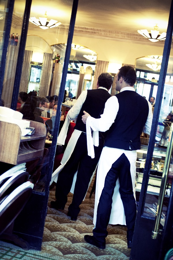 Two waiters in black withlong white aprons going through a door in a Paris restaurants; back view