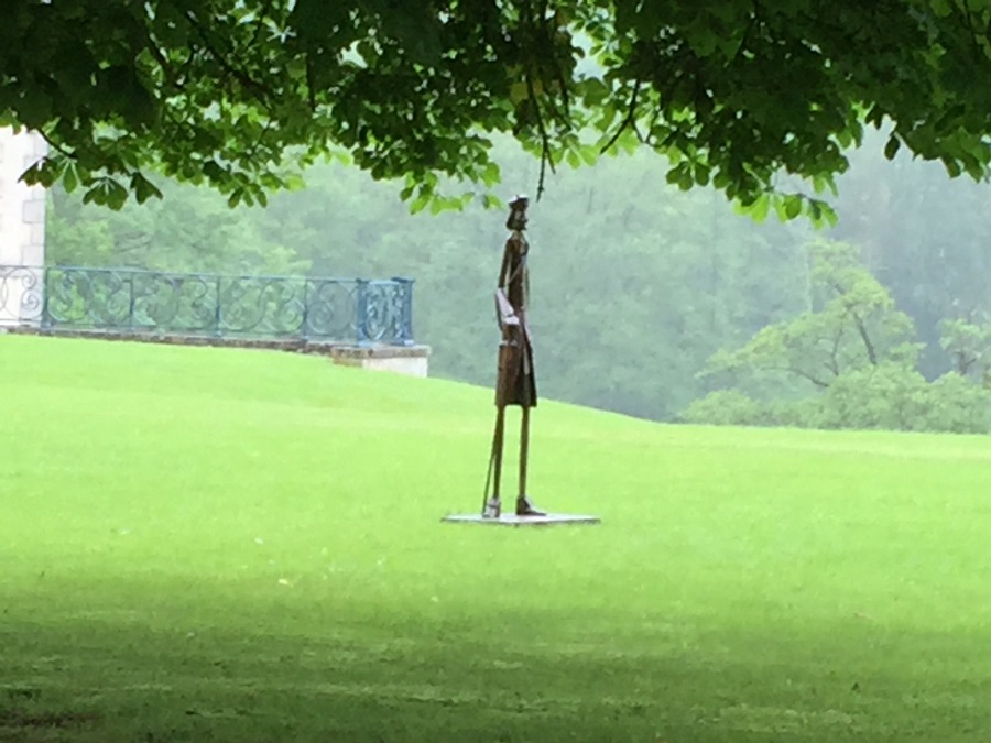 Thin, tall metal statue of abstract man in green park of chateau de Cirey