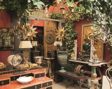 Puces de Saint-Ouen flea market in Paris with small shop full of orange/green/brown antiques from old lamps and urns to mirrors and clocks and furniture