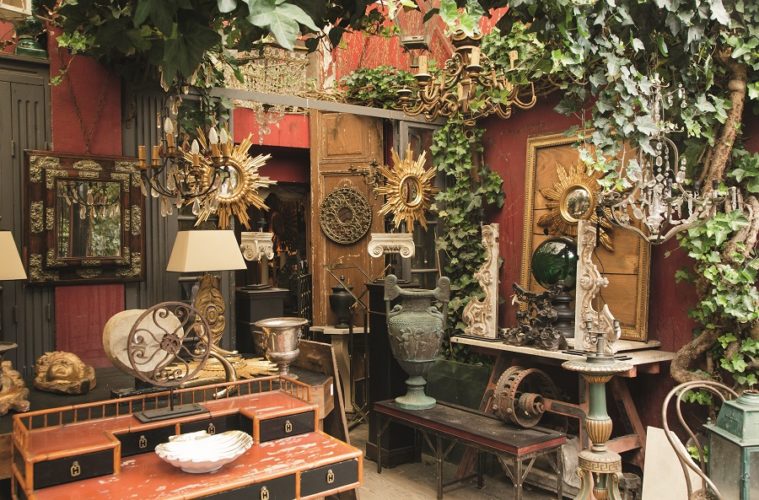 Puces de Saint-Ouen flea market in Paris with small shop full of orange/green/brown antiques from old lamps and urns to mirrors and clocks and furniture