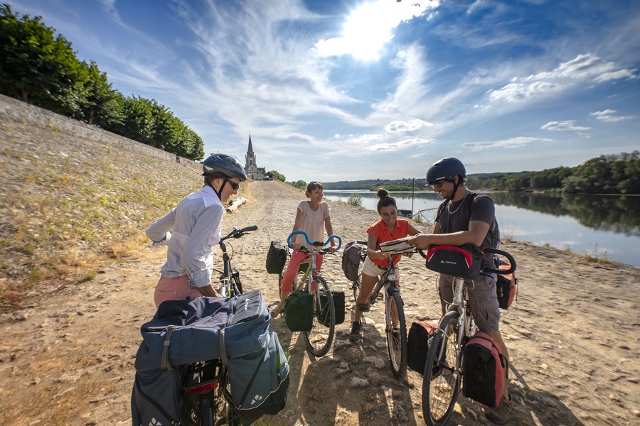 Two groups of cyclists, 4 people together on banks of the Loire on sand, with bicucles, talking and discussing route with maps