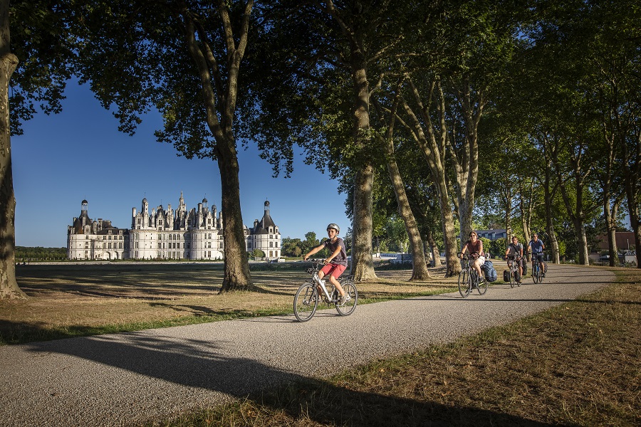 Chambord chateau, white stoned in background in park with cyclists on path in front